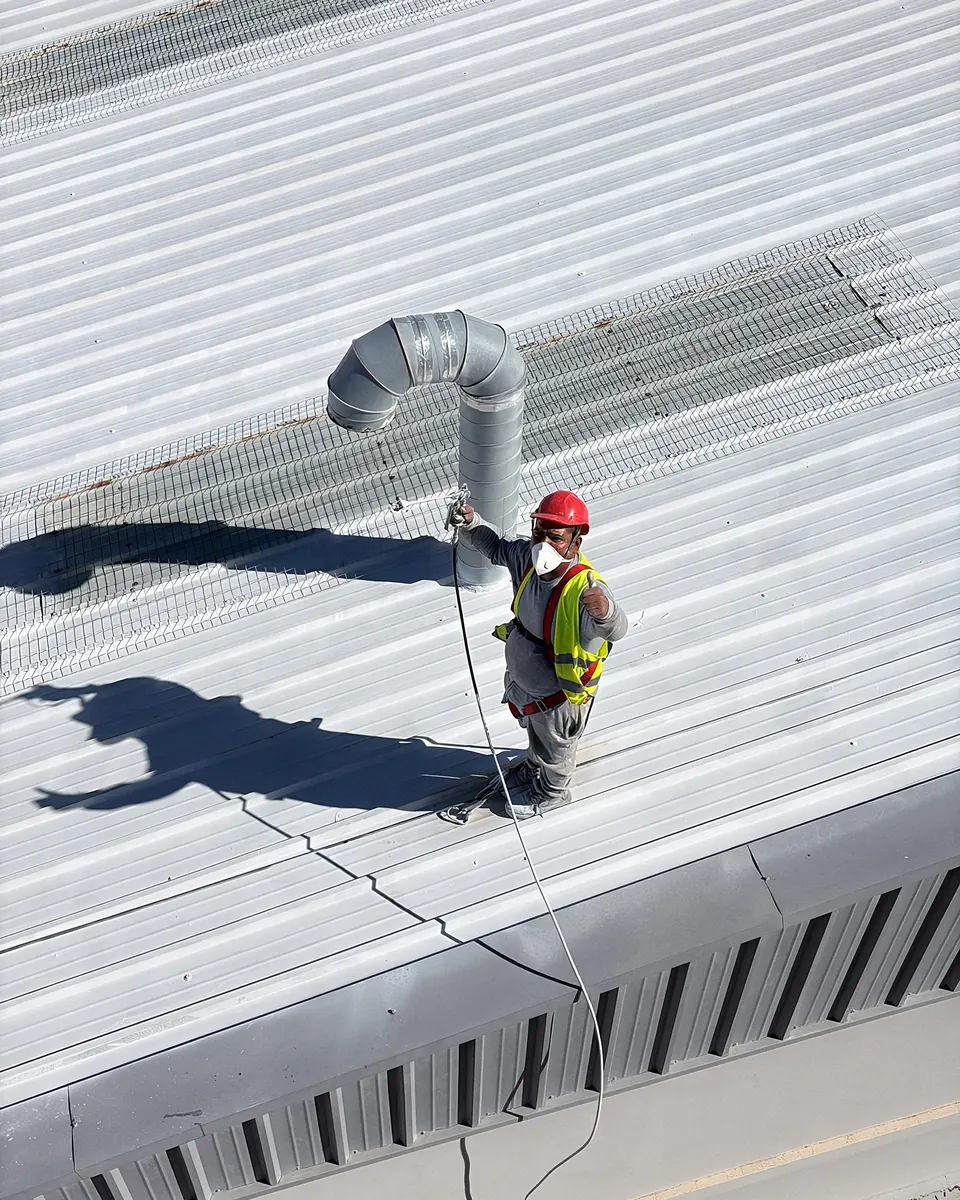 Operario de Imperion Tecpro aplicando el sistema termorreflectante junto a una chimenea de ventilación sobre la cubierta blanca de una nave industrial